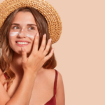 woman in straw hat applying sunscreen to her face