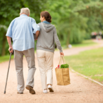 woman carrying shopping bag walking with an elderly man with a cane